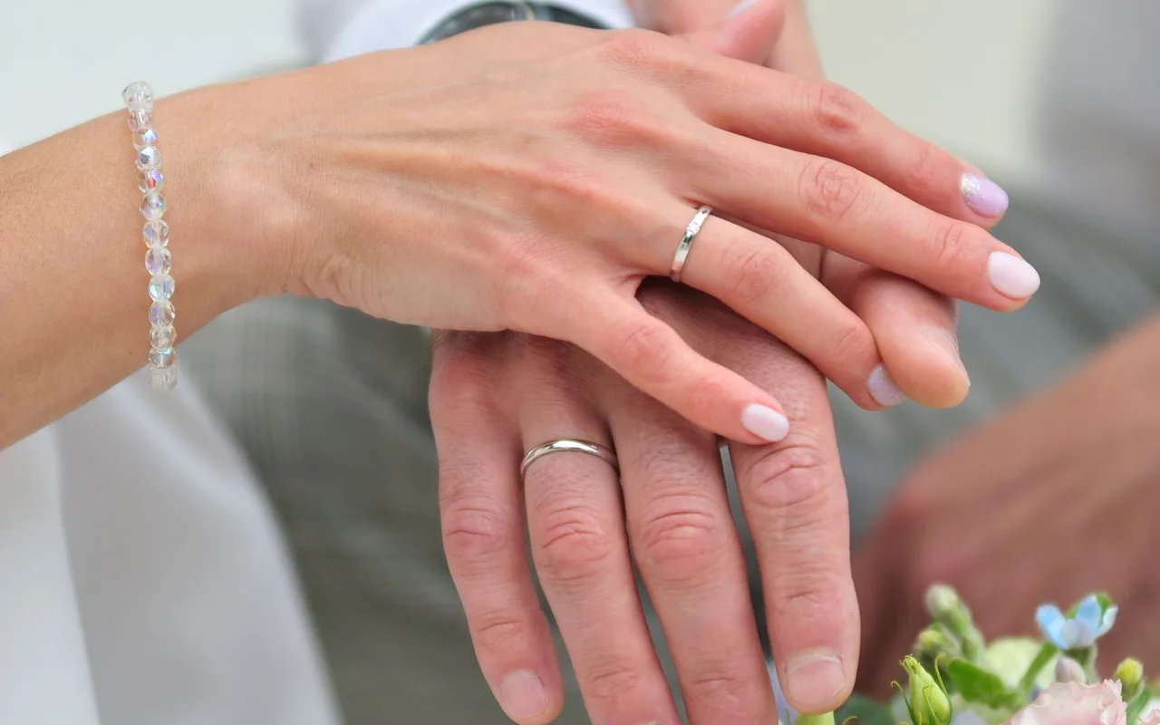 Tangan pasangan dengan cincin pernikahan di atas buket bunga.